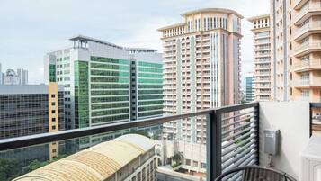 A balcony with a glass table and chairs, overlooking a cityscape with modern buildings.