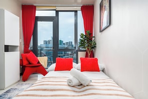 A hotel room with a bed, red pillows, a potted plant, and a city view. - The Florence Venice Mall Modern 1BR w/Balcony View (Taguig)