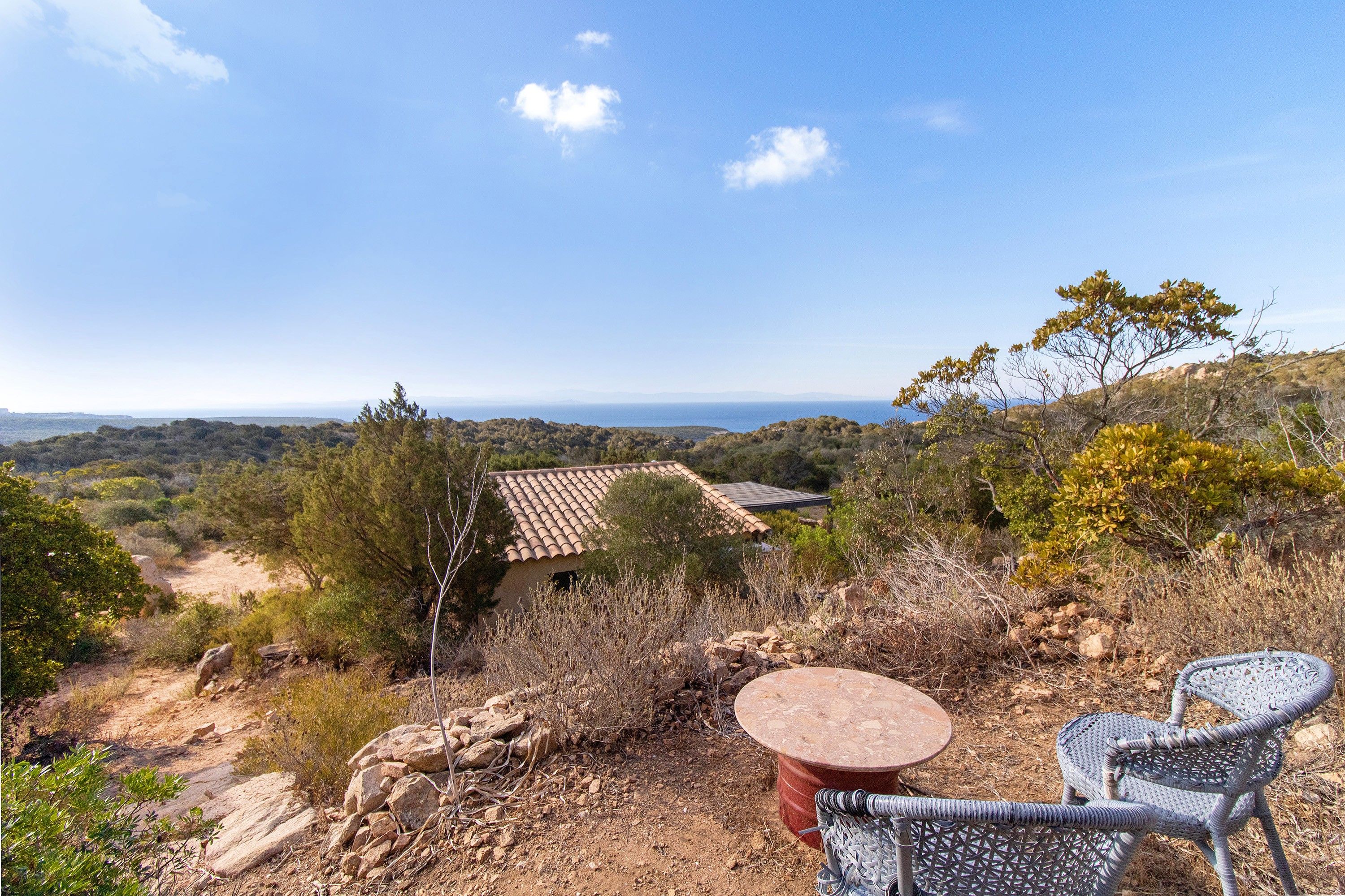 A patio with a table and chairs overlooking a mountainous landscape with a view of the sea.