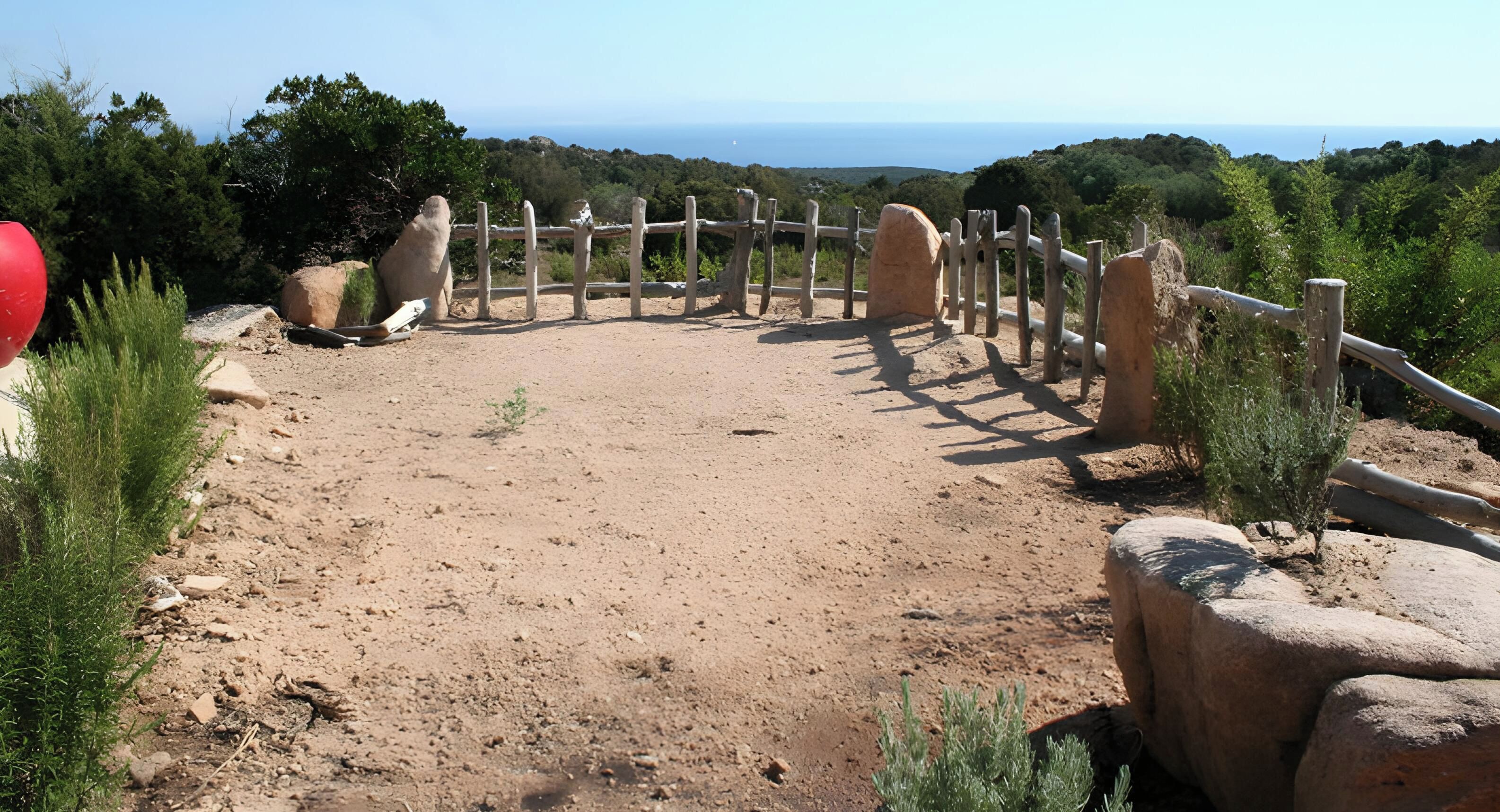 A dirt path leading to a wooden gate with a view of the sea in the background.