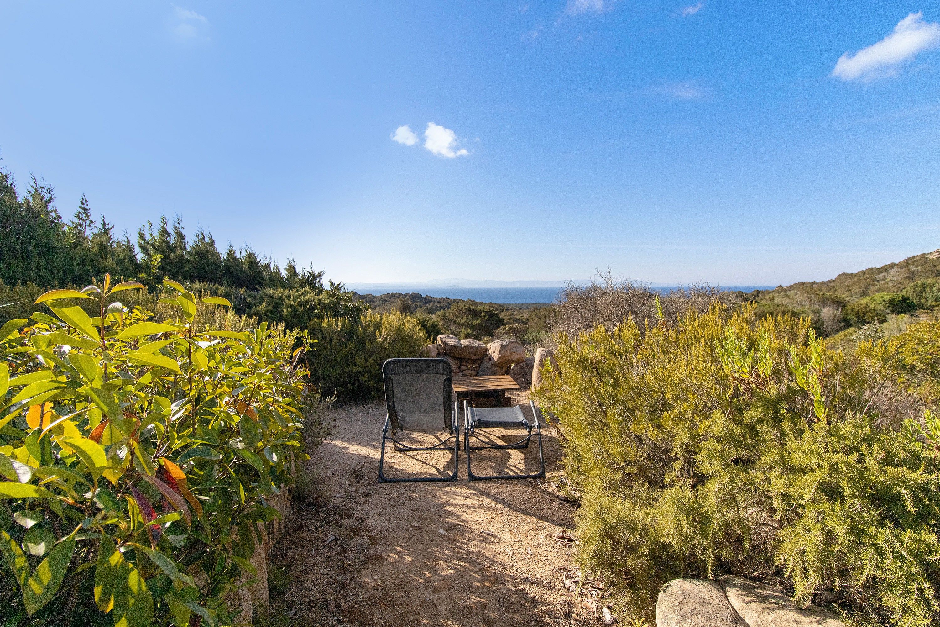 Un cadre naturel en plein air offrant une vue dégagée sur l’horizon, un espace de repos avec une chaise et une table, et un sentier de terre.