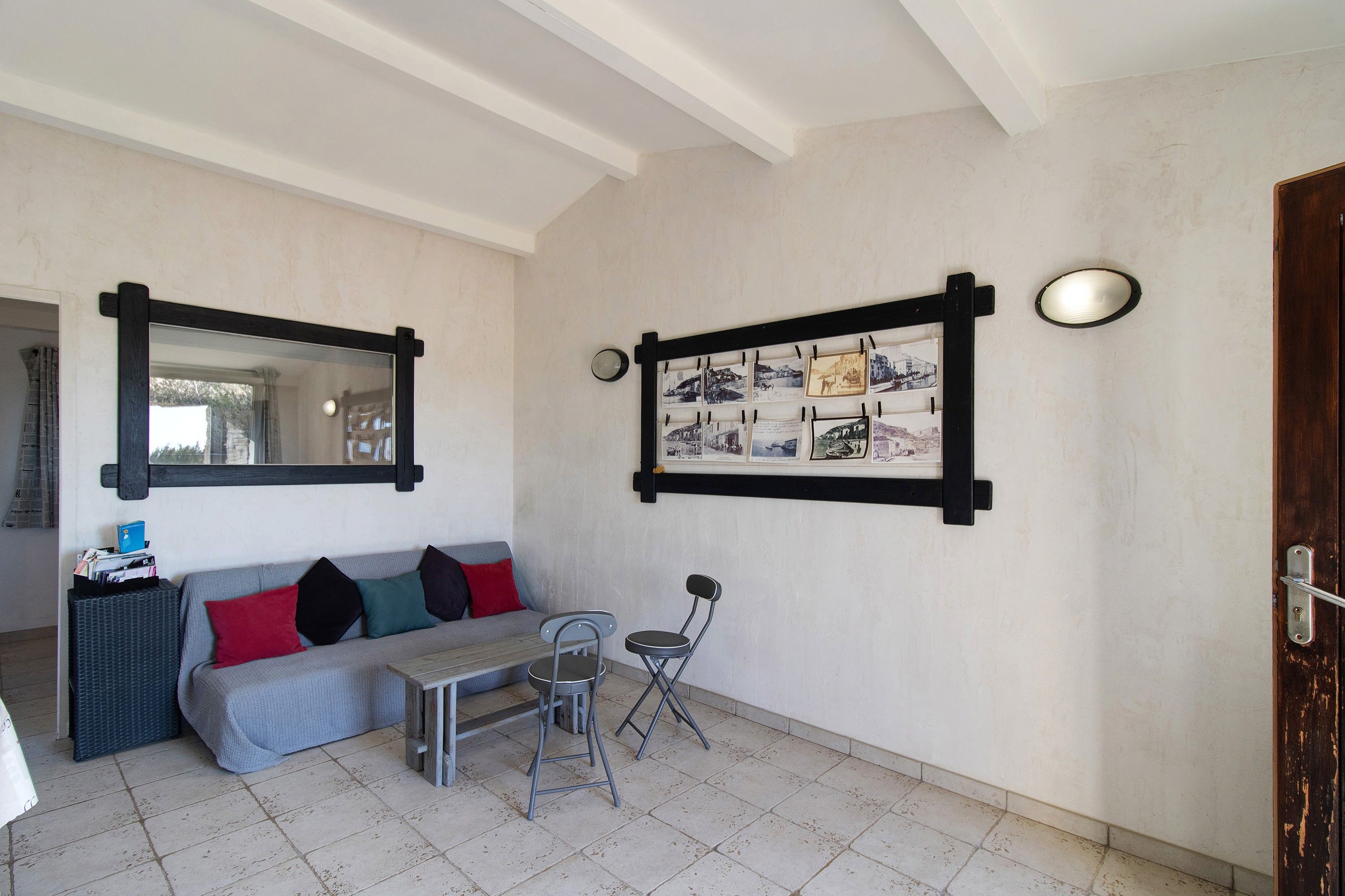 Une pièce avec un canapé gris, une petite table, une chaise, un miroir et un cadre photo fixé au mur.