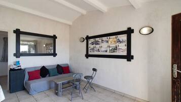 Une pièce avec un canapé gris, une petite table, une chaise, un miroir et un cadre photo fixé au mur.
