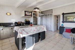 A compact kitchen with a dining table, a sofa, and a window with curtains. - Holiday Home 'La Bergerie' with Sea View, Wi-Fi and Air Conditioning (Bonifacio)