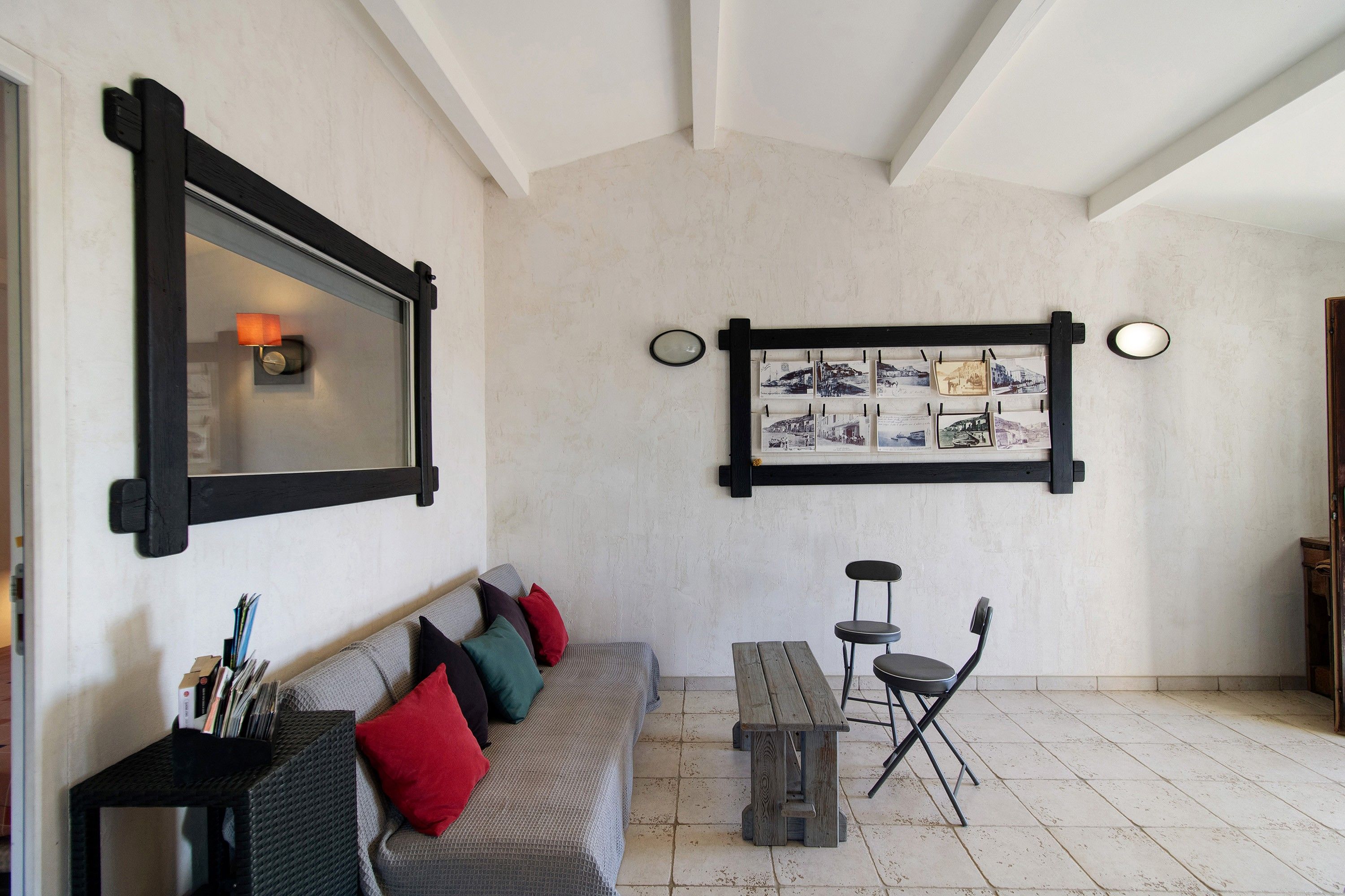 A room with a grey sofa, a wooden bench, and a table with chairs. There is a wall-mounted picture frame with multiple photographs.