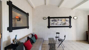 A room with a grey sofa, a wooden bench, and a table with chairs. There is a wall-mounted picture frame with multiple photographs.