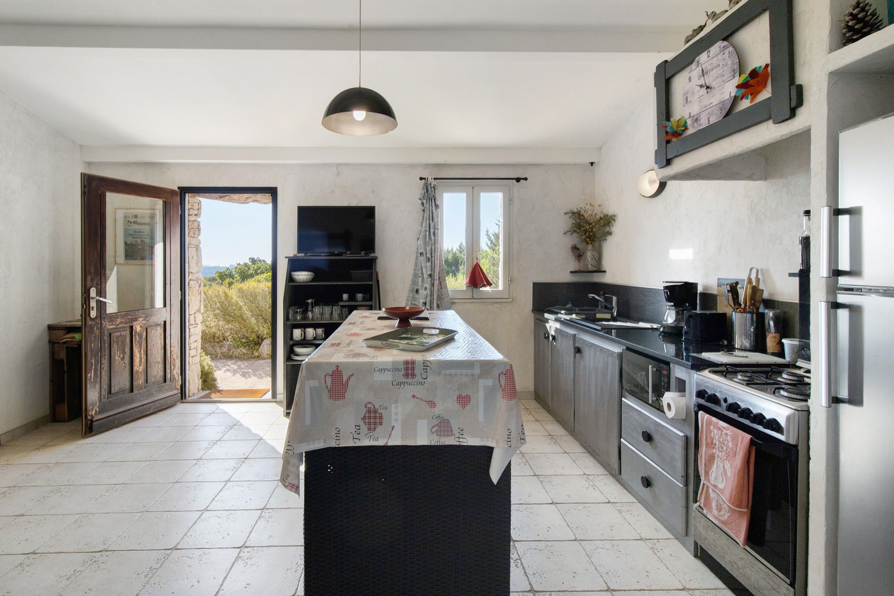 Een keuken met een centraal eiland, een kookplaat en een spoelbak. Er is een deur naar een buitenruimte.