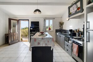 A kitchen with a central island, a stove, and a sink. There is a door leading to an outdoor area. - Holiday Home 'La Bergerie' with Sea View, Wi-Fi and Air Conditioning (Bonifacio)