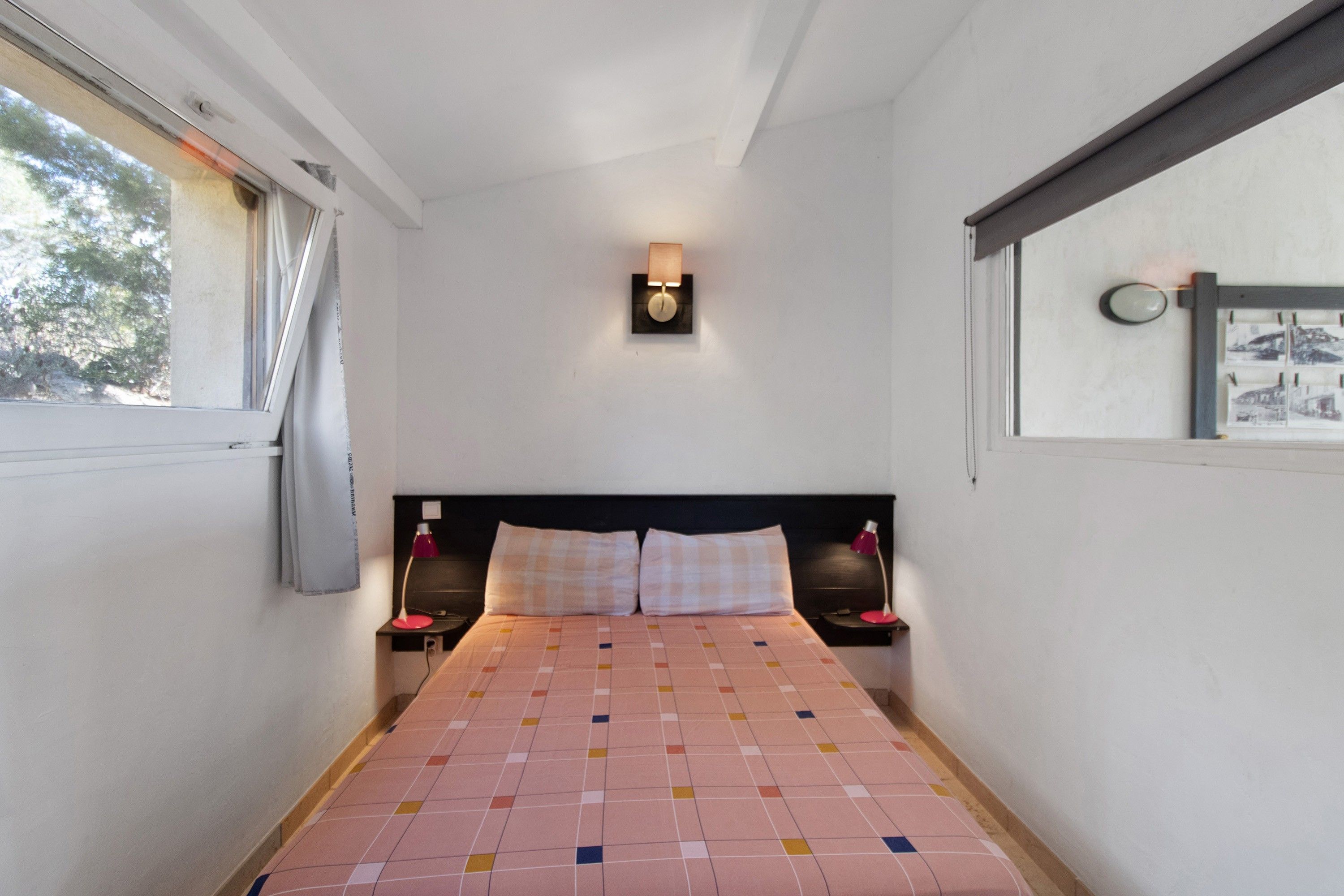 Een smalle hotelkamer met een bed, twee nachtkastjes, een wandlamp en een raam met gordijnen.