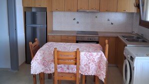 A kitchen with wooden cabinets, a stainless steel refrigerator, a table with chairs, a washing machine, and a window. - Apartment 'Porto Beach' with Sea View, Wi-Fi and Air Conditioning (Makry Gialos)