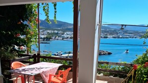 Área de estar coberta ao ar livre, com mesa e cadeiras, com vista para um corpo d'água e uma cidade distante.