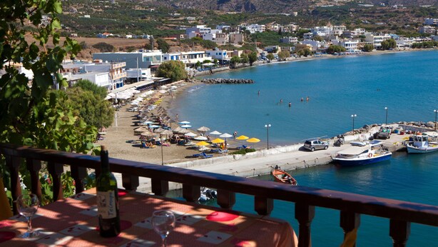 Uma vila costeira com praia, barcos e uma mesa com garrafa e copos.