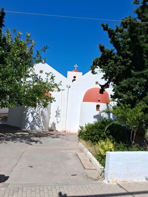 Un edificio blanco con una cúpula roja y una cruz en la parte superior, rodeado de follaje.
