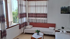 Quarto de hotel com cama, sofá, mesa com uma planta, televisão e janela com cortinas.