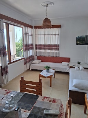 Ein Hotelzimmer mit einem Bett, einer Couch, einem Tisch mit Pflanze, einem Fernseher und einem Fenster mit Vorhängen.