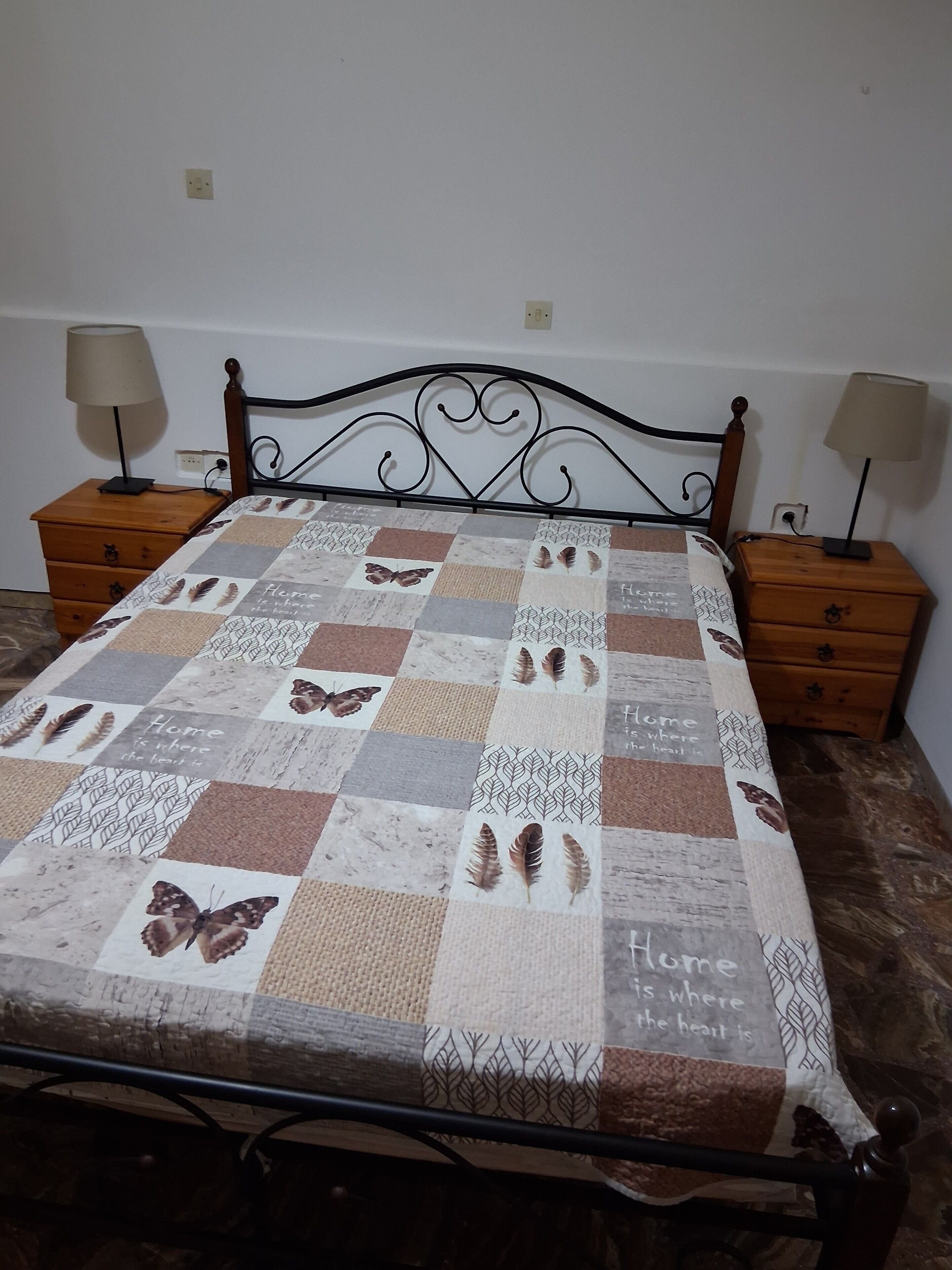 A bed with a quilt featuring butterfly patterns and the phrase 'Home is where the heart is.'