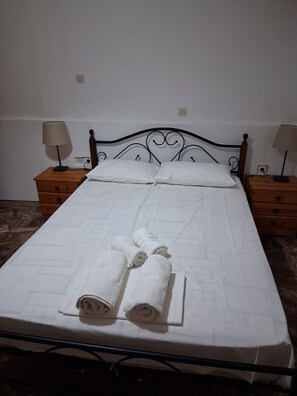 Een net opgemaakt bed met witte linnens en opgerolde handdoeken, twee nachtkastjes met lampen, en een marmeren vloer.