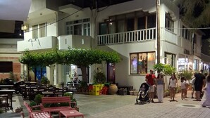 Uma área de estar externa com mesas e bancos, cercada por edifícios com sacadas e janelas.