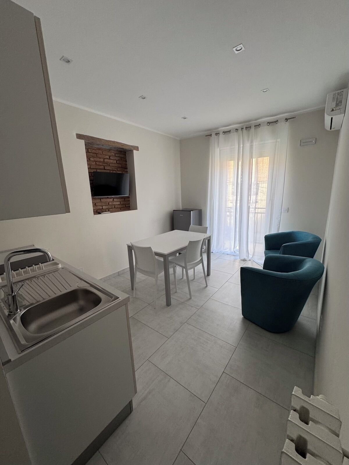 Une cuisine moderne dotée d’un four encastré, un coin repas avec une table et des chaises, et un espace détente avec un fauteuil bleu.