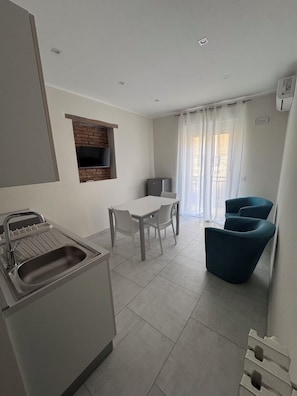 Una cuina moderna amb forn integrat, zona de menjador amb taula i cadires, i zona de seients amb una cadira blava.