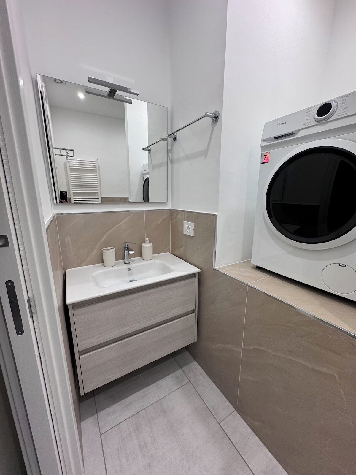 Ein modernes Badezimmer mit Waschbecken, Spiegel, Handtuchhalter und einer integrierten Waschmaschine.