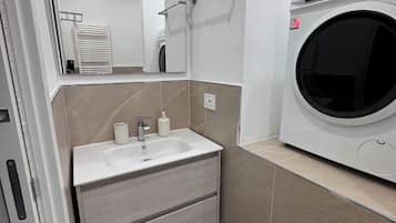 Ein modernes Badezimmer mit Waschbecken, Spiegel, Handtuchhalter und einer integrierten Waschmaschine.