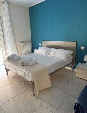 Ein Hotelzimmer mit Bett, Nachttisch, Lampe und Blick ins Freie.