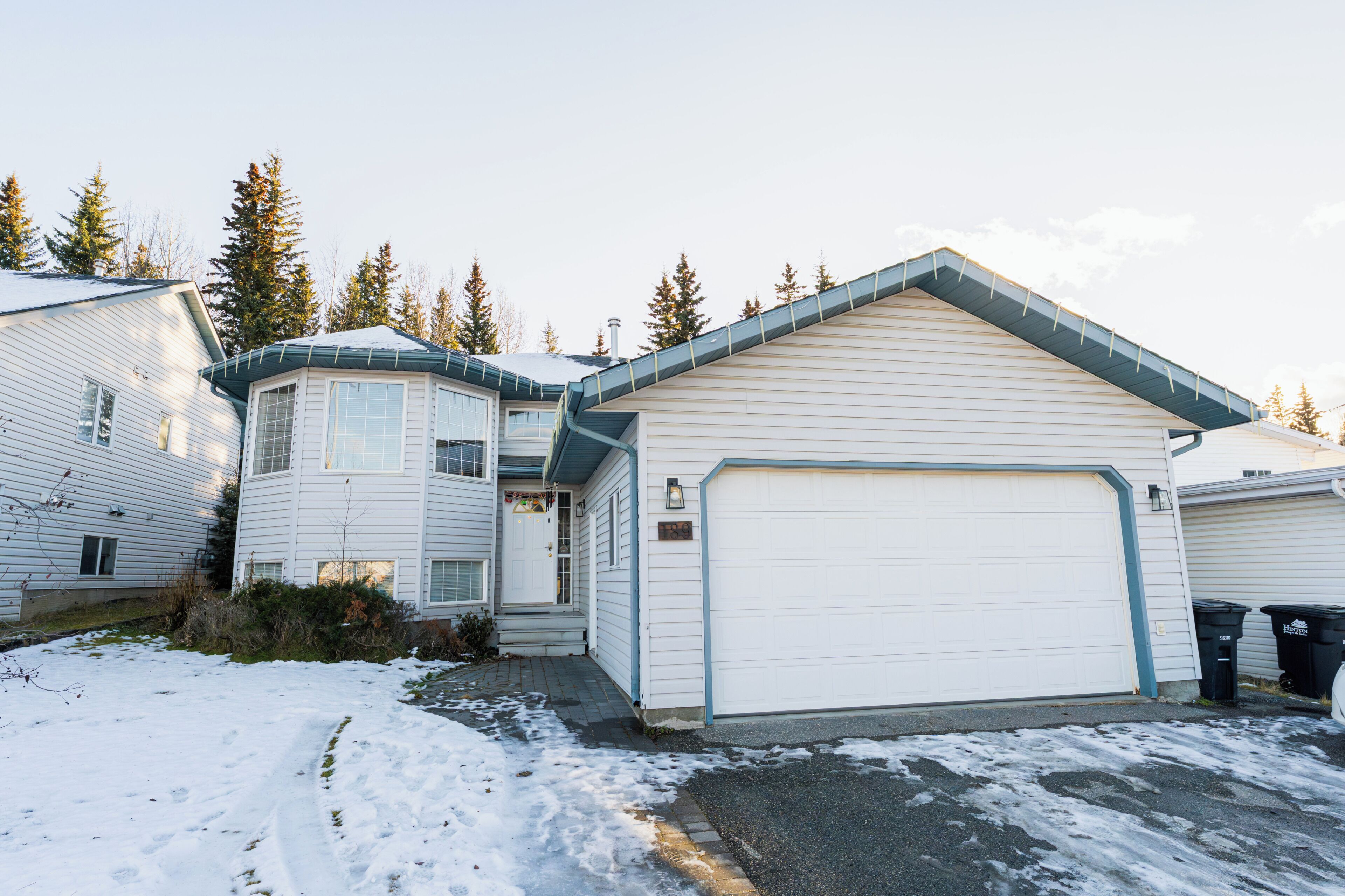 A residential property with a detached garage, a covered porch, and a snow-covered driveway.