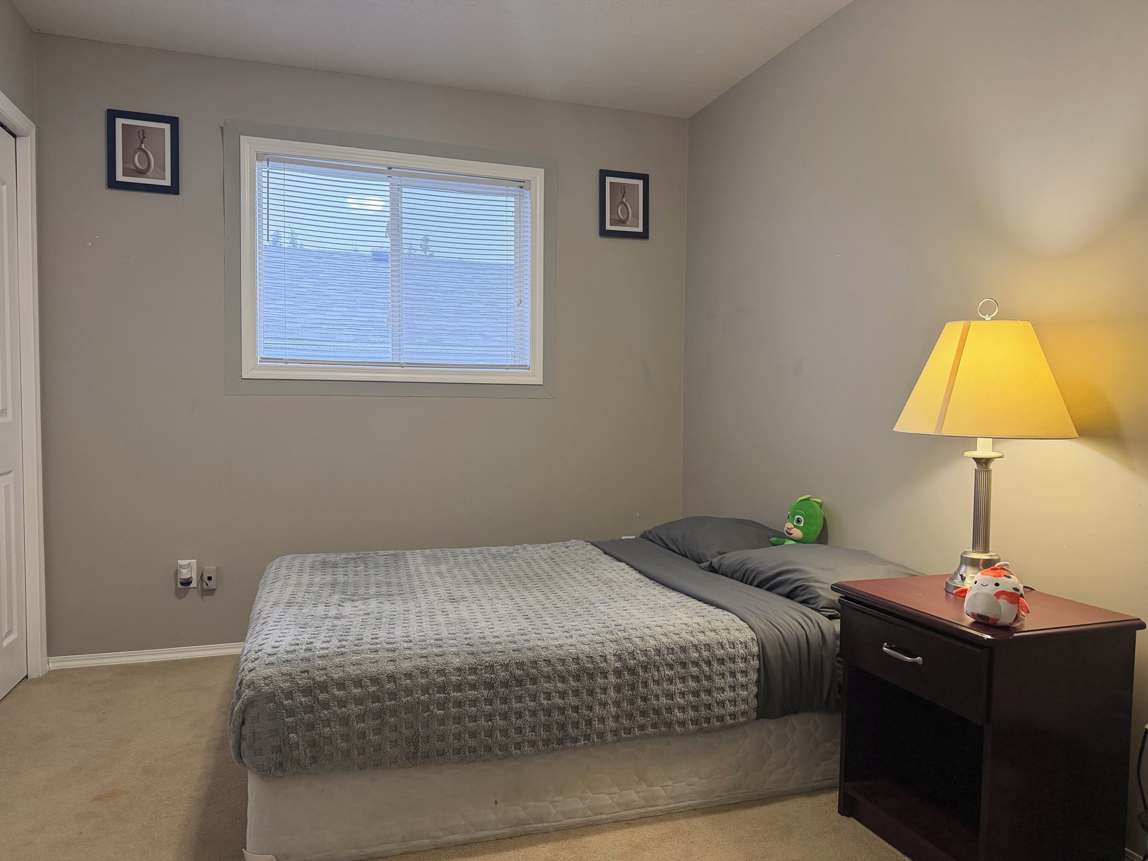 A bedroom with a bed, a window with blinds, a lamp, and a dresser.