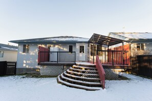 Ett bostadshus med en veranda framför, en trappa som leder upp till entrén och en snötäckt trädgård.