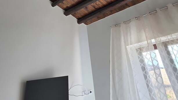 Una stanza con soffitto in legno, TV a schermo piatto montata a parete e finestra con tende leggere.