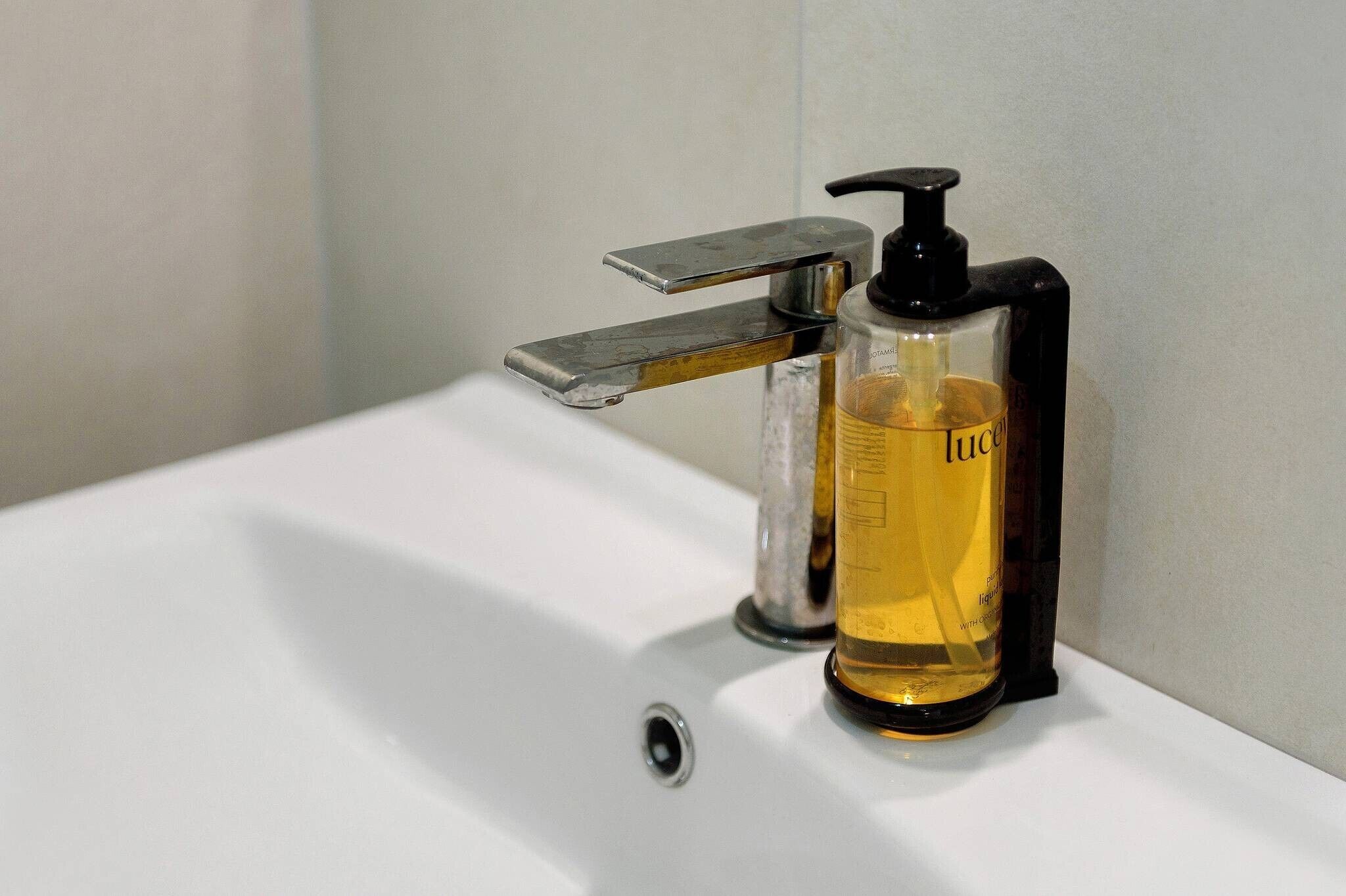 Un lavabo de bany amb aixeta i una ampolla de sabó líquid.