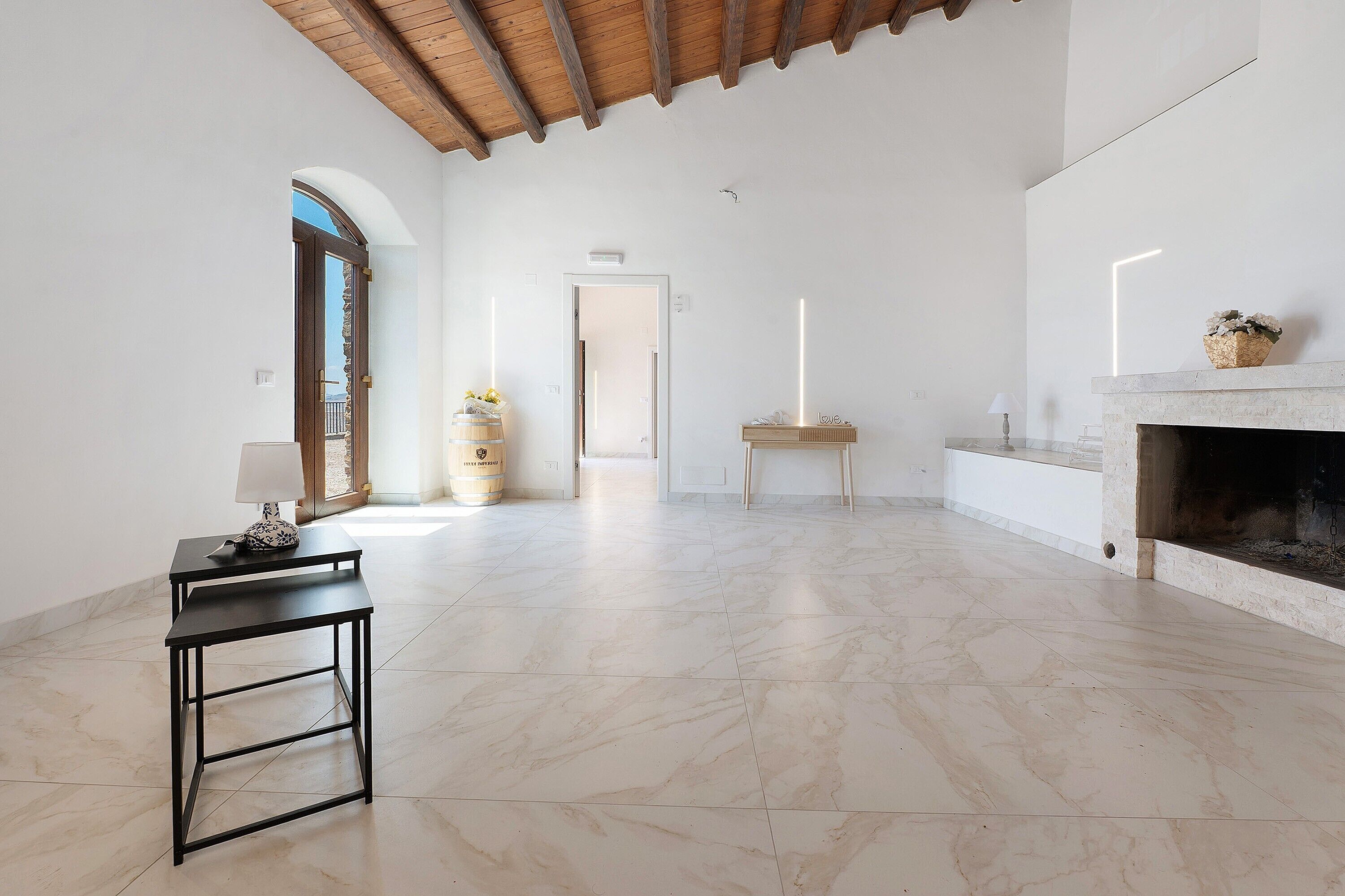 A spacious room with a marble floor, a fireplace, a table with a lamp, and a door leading to another area.