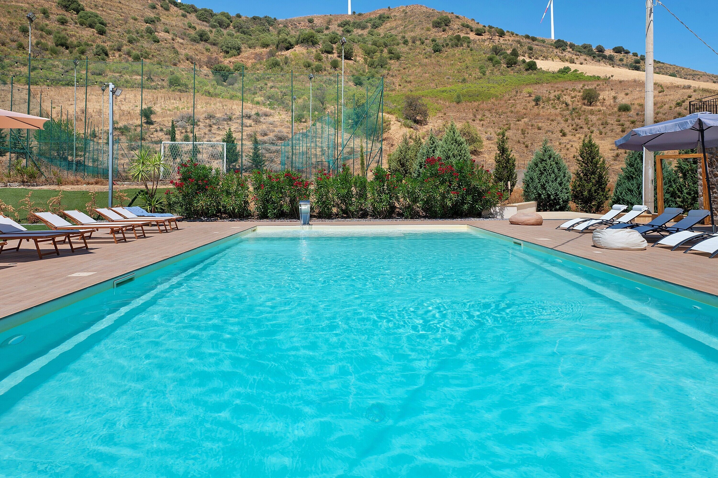 A clear blue pool with lounge chairs and a view of a hilly landscape.