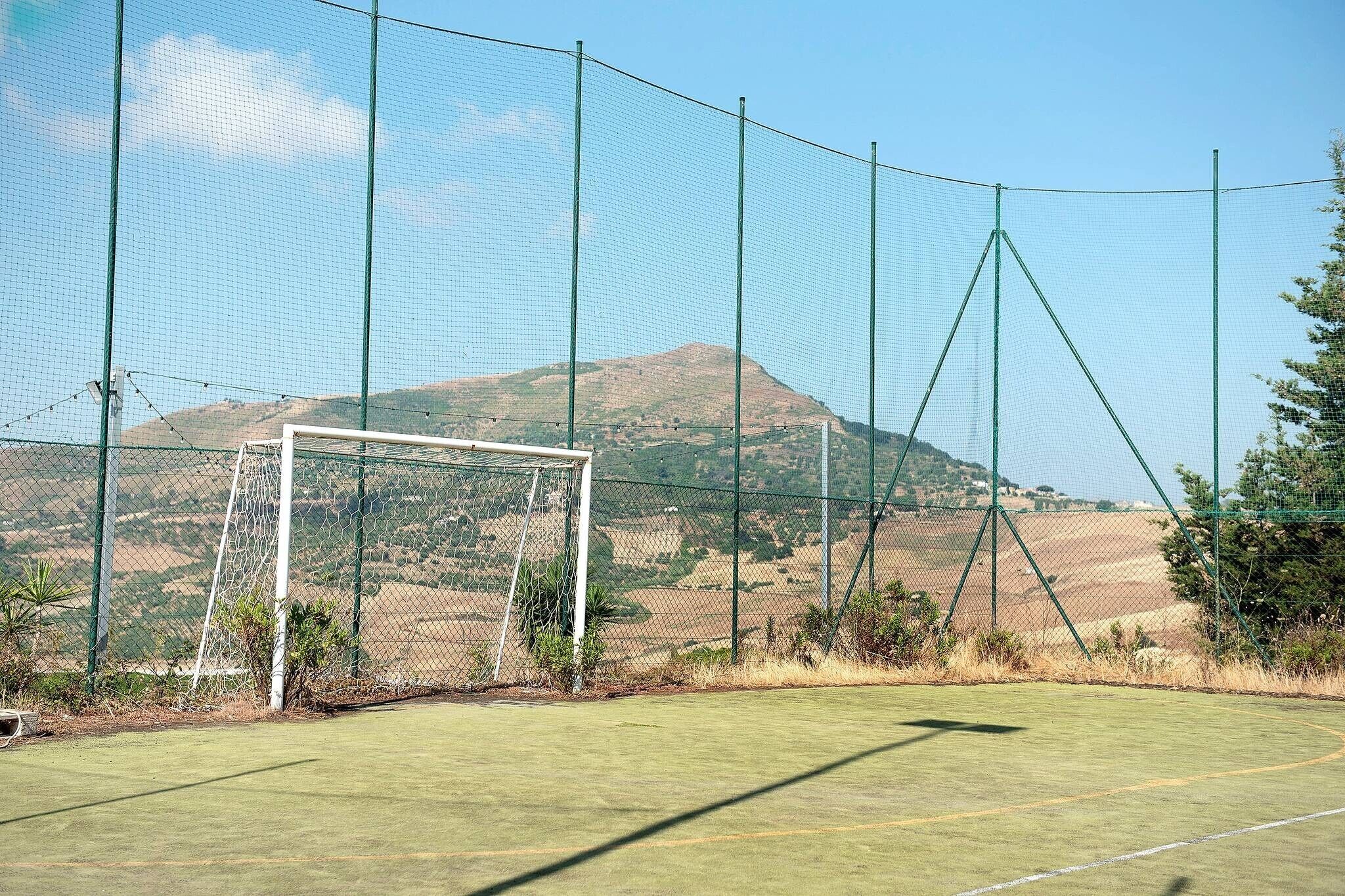 Un campo de fútbol con un poste de portería y una cerca de malla, rodeado por un paisaje montañoso.