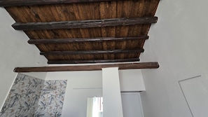 Una habitació amb estructura de sostre de fusta, parets blanques i paper pintat amb motius florals.