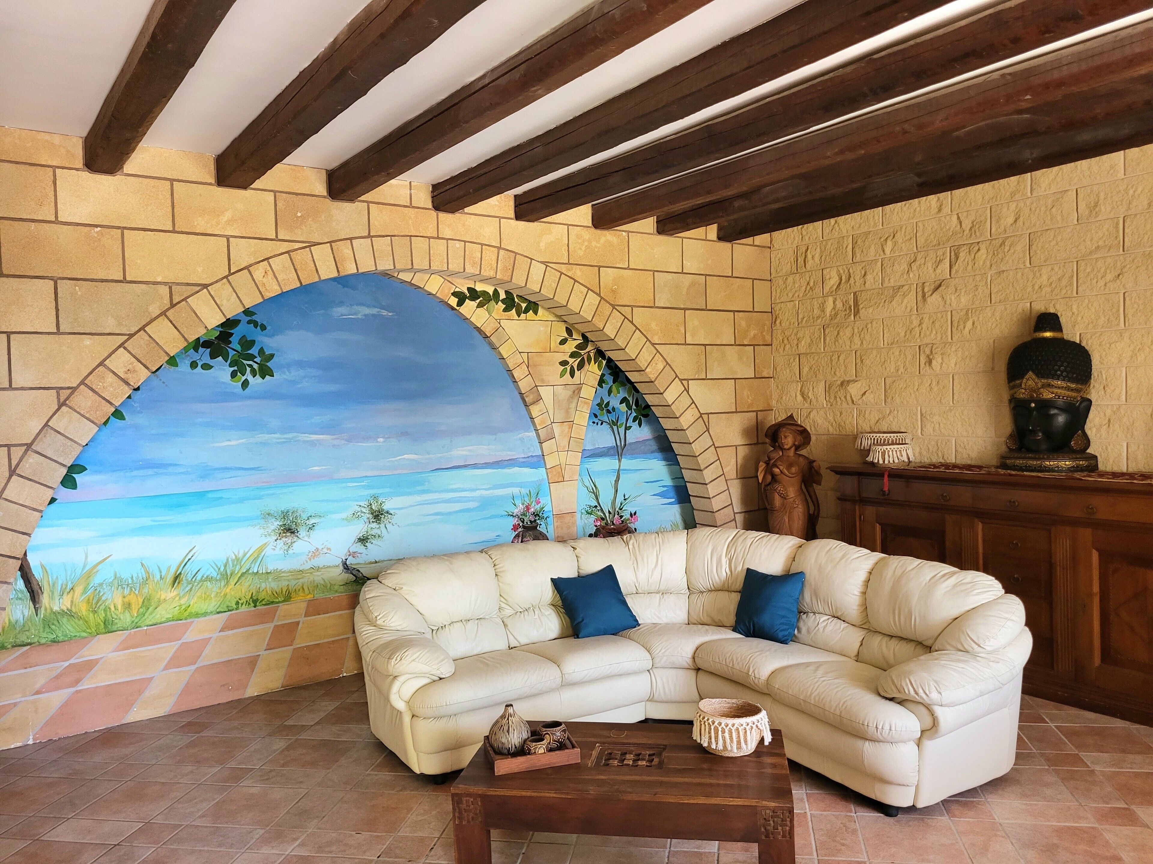 Ein Wohnzimmer mit einem weißen Ledersofa, einem Couchtisch und einem Wandbild mit Strandmotiv.