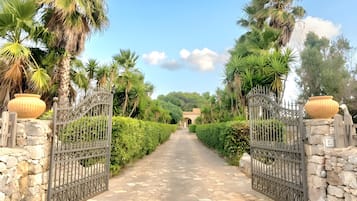 A paved pathway leading to a gated entrance with stone walls and decorative metal gates.