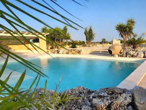A swimming pool with a stone structure, palm trees, and a clear sky. - SeaShell – Salento Retreat: Private Pool, Wi-Fi & A/C, 1 km from the Sea (Corsano)