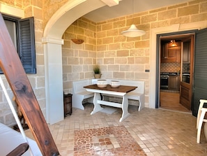 A stone-walled room with a wooden bench, a hanging light fixture, and a view into the kitchen. - SeaShell – Salento Retreat: Private Pool, Wi-Fi & A/C, 1 km from the Sea (Corsano)