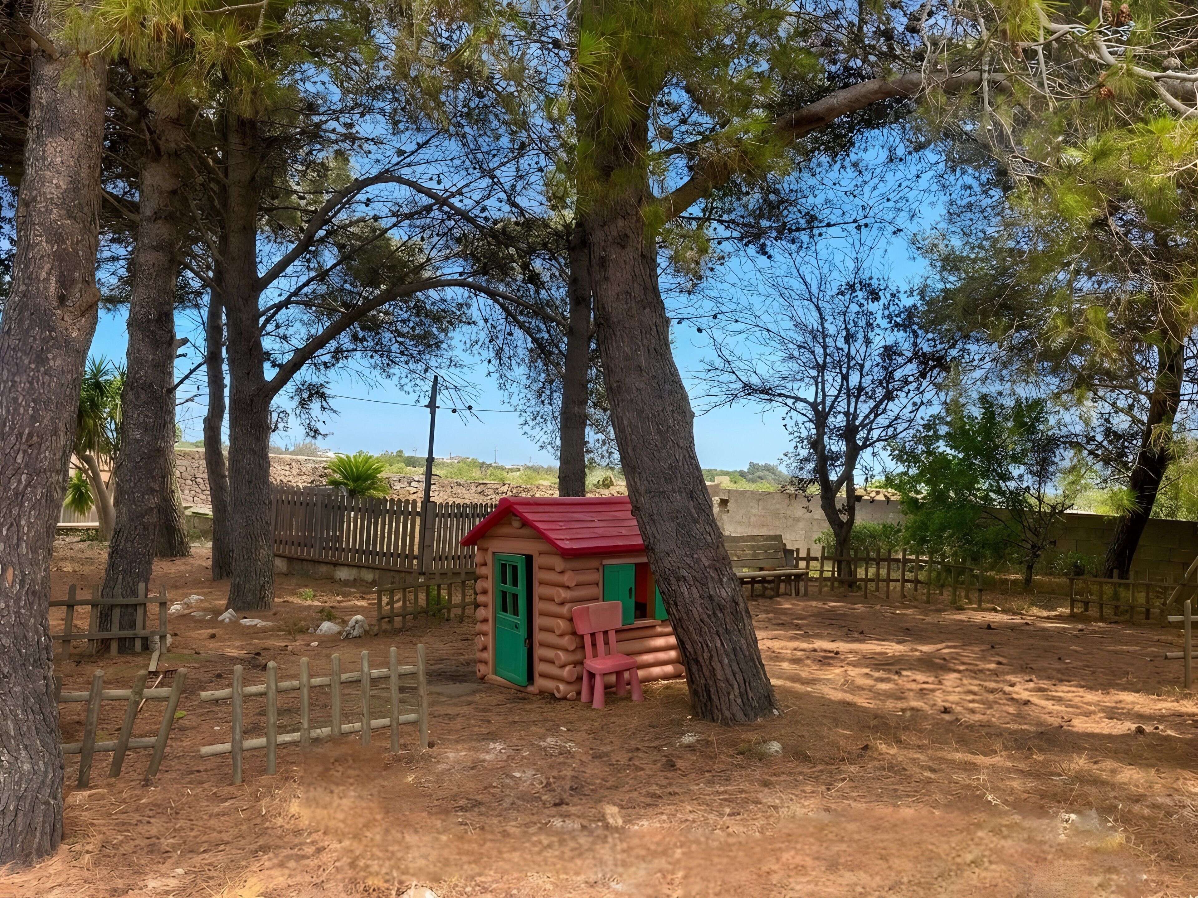Un rustico chalet con tetto rosso e porta verde, immerso tra alberi alti e circondato da una recinzione in legno.