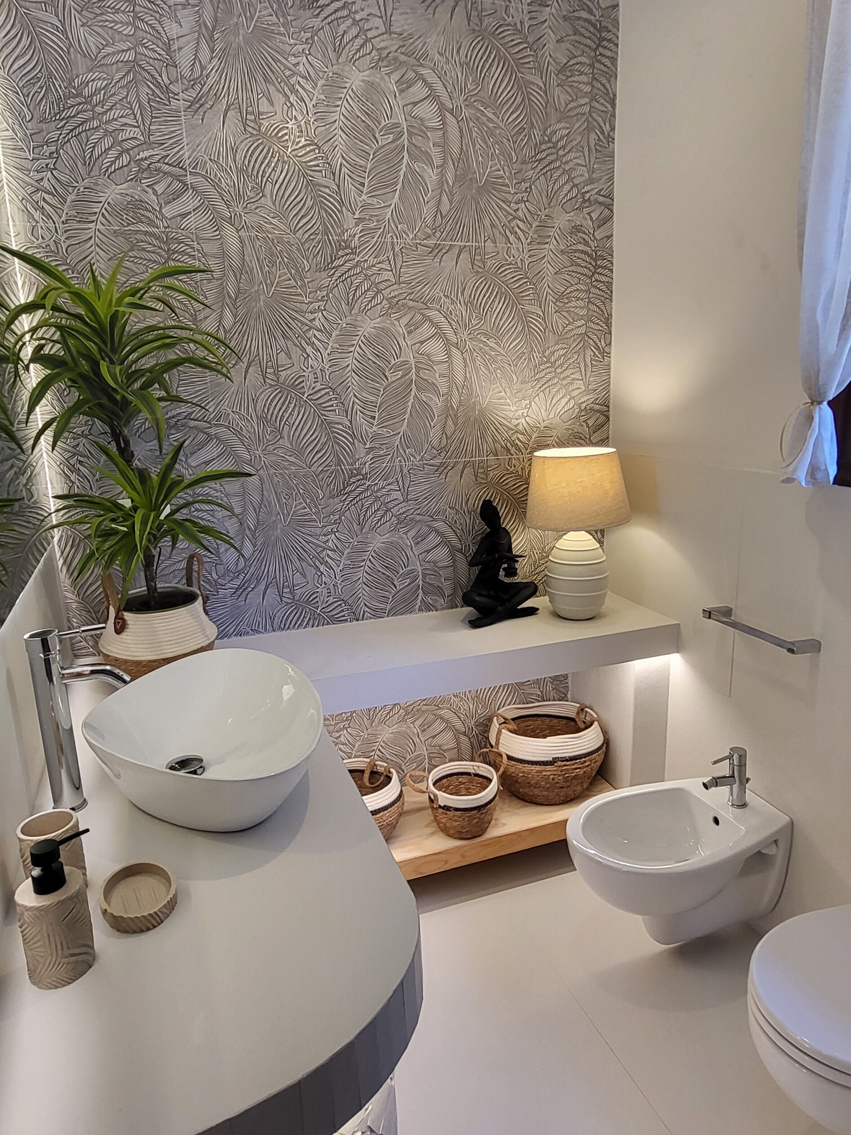A modern bathroom with a white sink, a vessel sink, a bidet, a toilet, a mirror, a shelf with decorative items, and a potted plant.