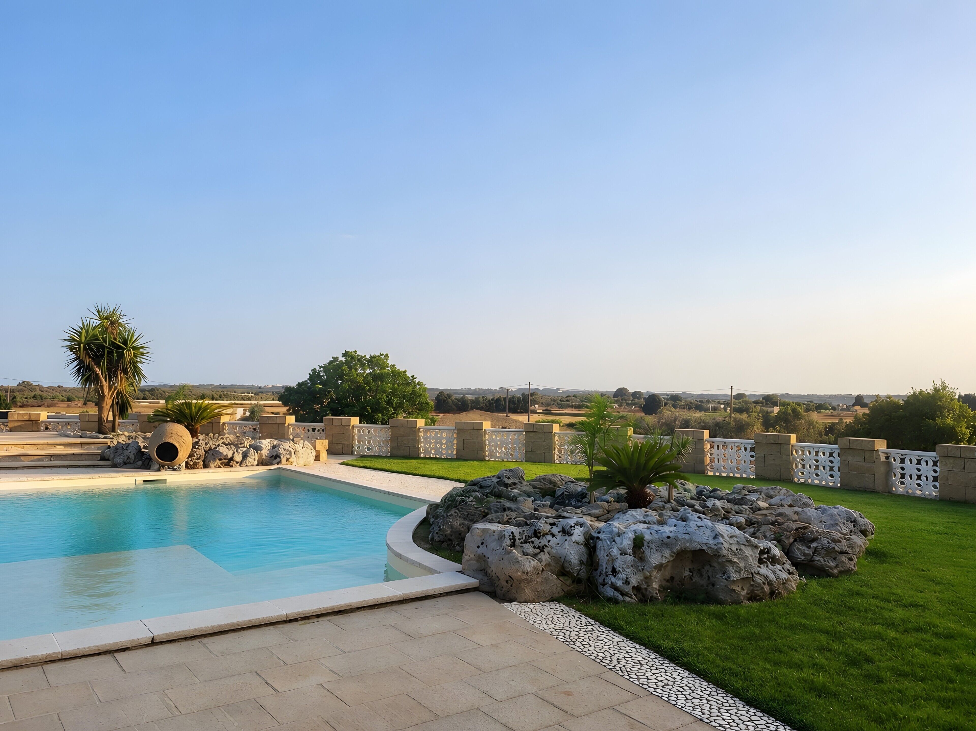 A swimming pool with a stone border, a grassy area, and a view of the countryside.