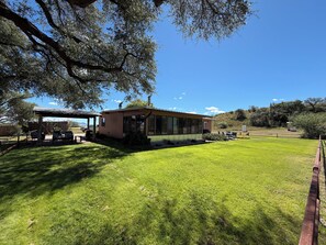 A house with a covered patio, a lawn, and a view of the surrounding landscape. - Beautiful 3-Bedroom Home in Sonoita Under the Oaks (Sonoita)