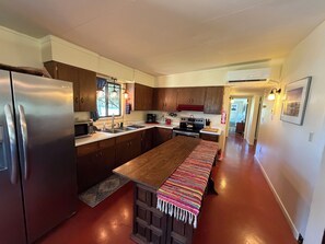 A kitchen with a central island, stainless steel appliances, wooden cabinets, and a red floor. - Beautiful 3-Bedroom Home in Sonoita Under the Oaks (Sonoita)