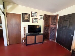A room with a television on a stand, a wooden door, and a wall with framed pictures. - Beautiful 3-Bedroom Home in Sonoita Under the Oaks (Sonoita)