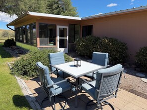 A patio with a table and four chairs, a small lantern, and a house with a sliding glass door. - Beautiful 3-Bedroom Home in Sonoita Under the Oaks (Sonoita)
