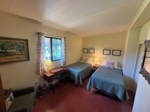 A room with two beds, a desk, a chair, a window with curtains, and framed pictures on the wall. - Beautiful 3-Bedroom Home in Sonoita Under the Oaks (Sonoita)