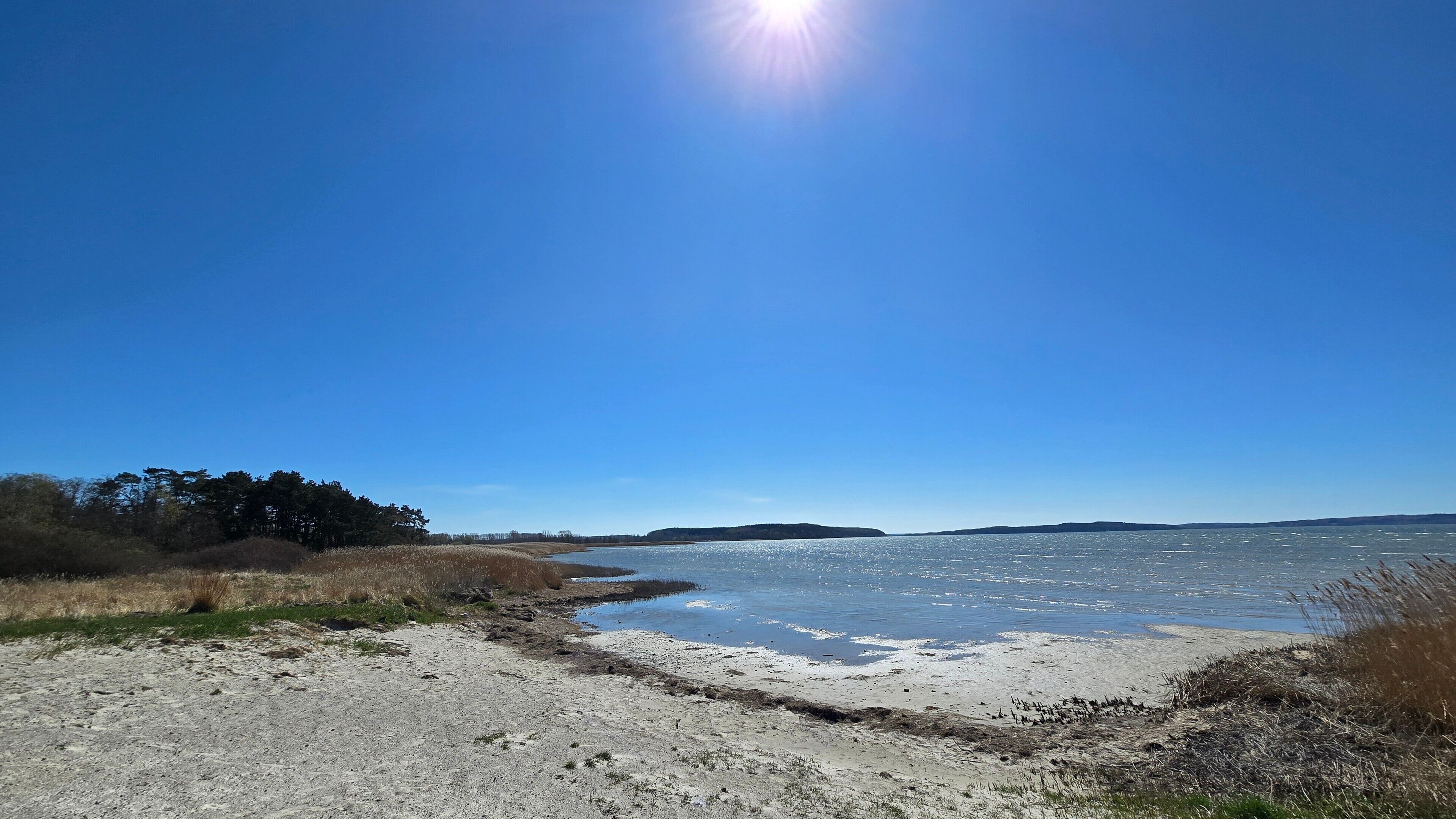En strand med klar himmel, sandet bredde og roligt vand.