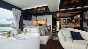 A modern interior with a large bathtub, a sofa, and a bed with a view of a yacht outside. - Houseboat 'Hafensuite Rügen' with Wi-Fi and Panoramic Views on Rügen Island (Sagard)